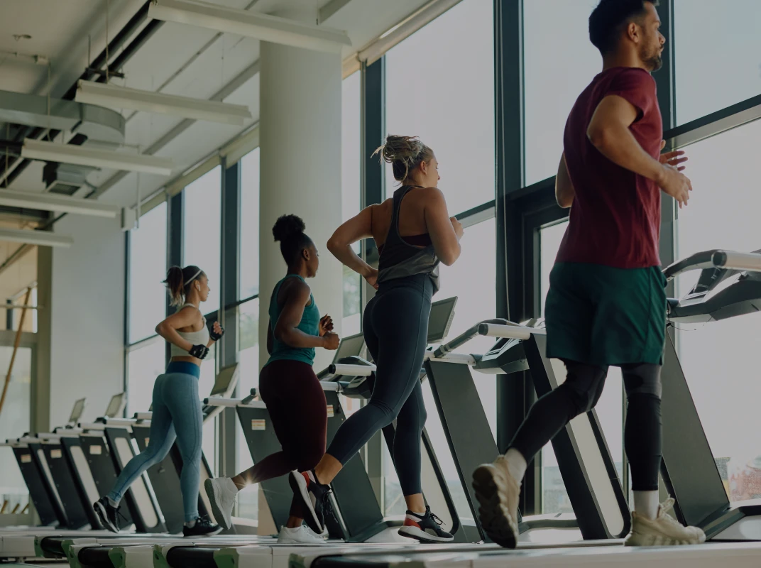 Three women running on treadmills in a bright, modern gym with large windows