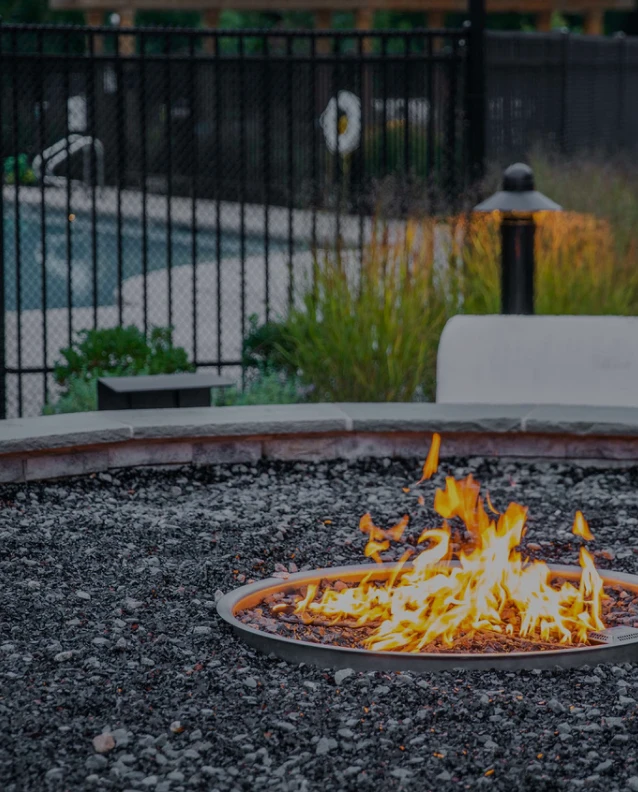 Outdoor fire pit with glowing flames surrounded by lava rocks and garden landscaping