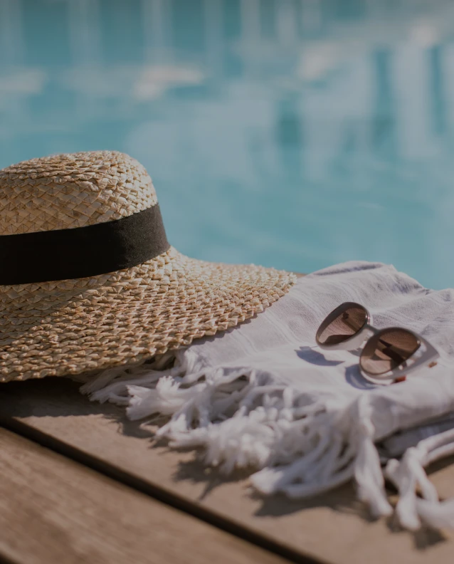 Poolside view with stylish beach hat, sunglasses, and white fringed towel on deck