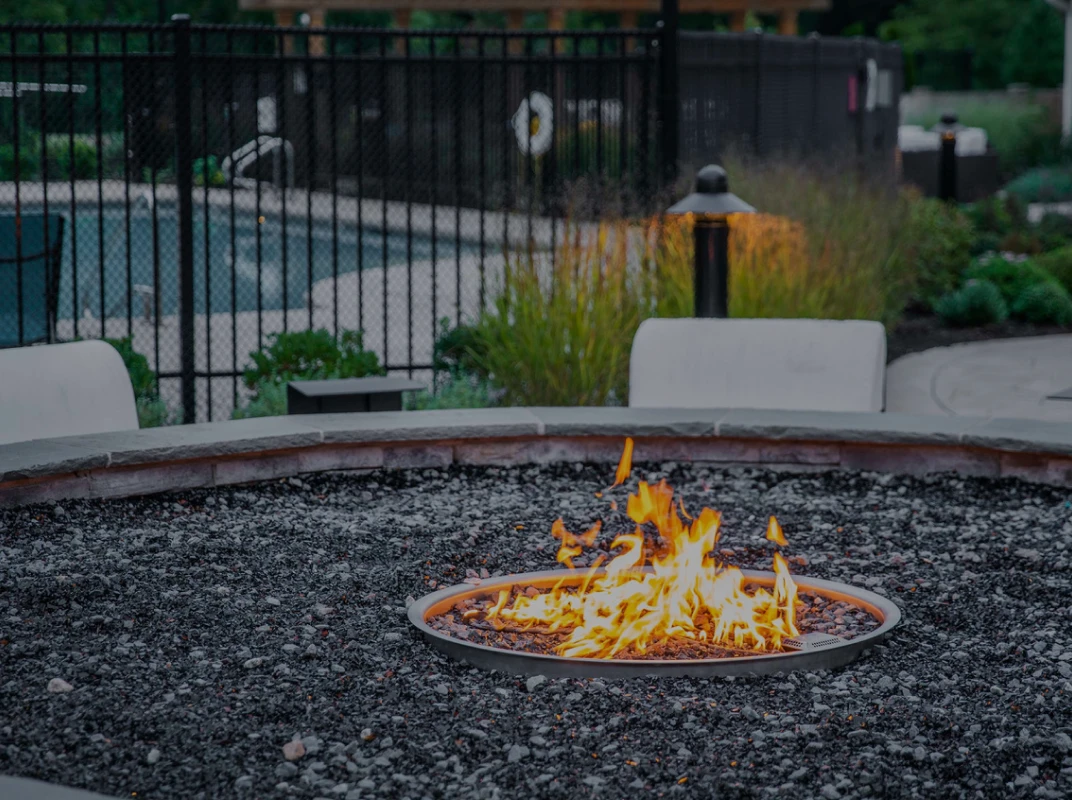 Modern firepit with flames surrounded by black gravel in landscaped outdoor setting