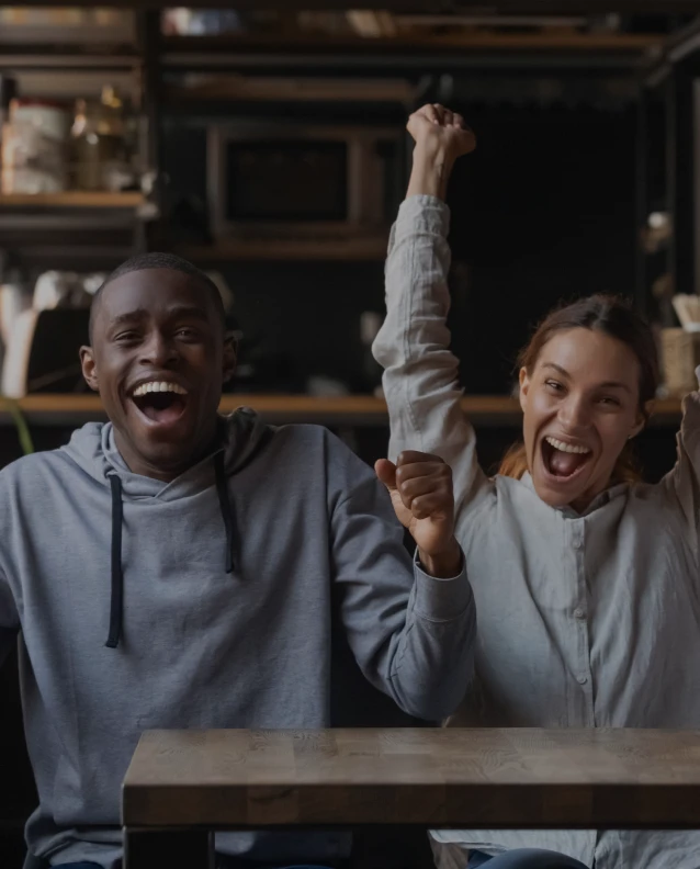 Man and woman celebrating with raised arms in casual bar or cafe setting