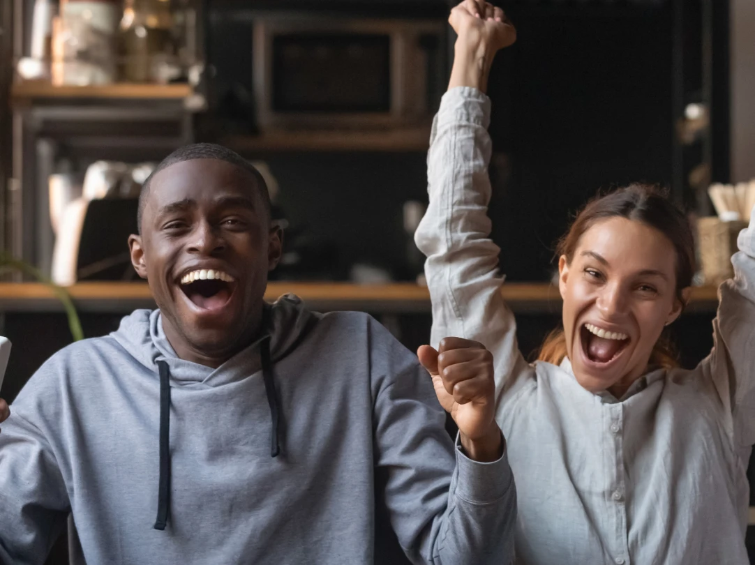 Man and woman celebrating with raised arms in casual bar or cafe setting