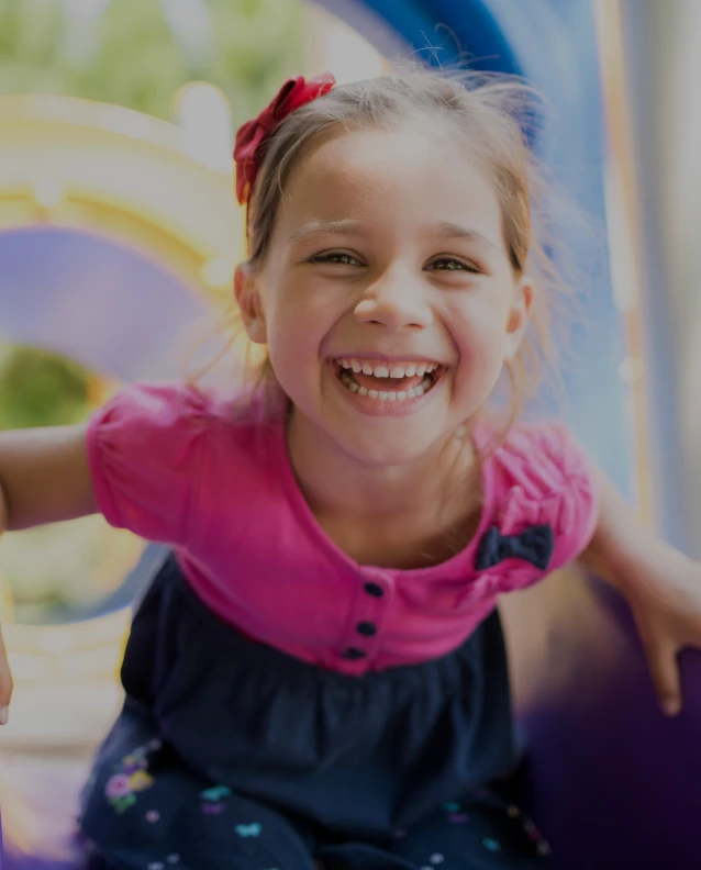 Happy young girl laughing while playing on colorful playground equipment in bright sunlight