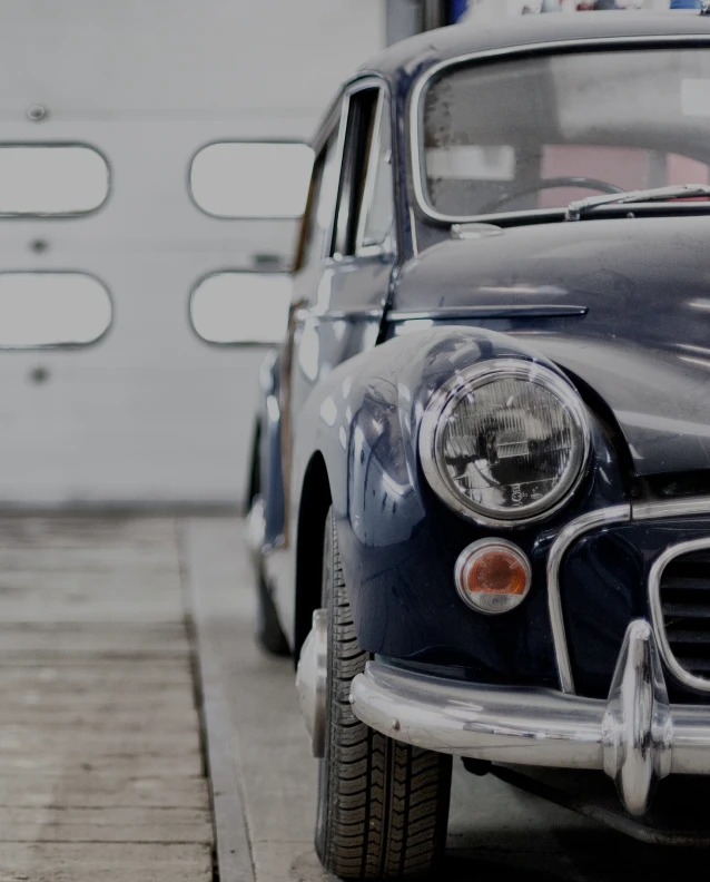 Classic dark blue vintage car parked inside garage with wood flooring and white doors