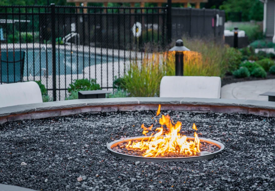 Outdoor firepit with cozy seating near landscaped pool area in apartment complex