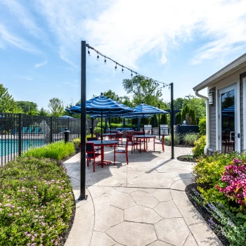 Tiled patio walkway with red seating, string lights, and landscaped flower beds near pool