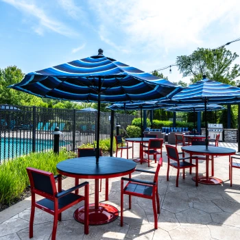 Poolside patio setup with red chairs and tables shaded by bold blue-striped umbrellas