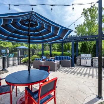 Covered barbecue area with two stainless steel grills and blue-striped lounge furniture nearby