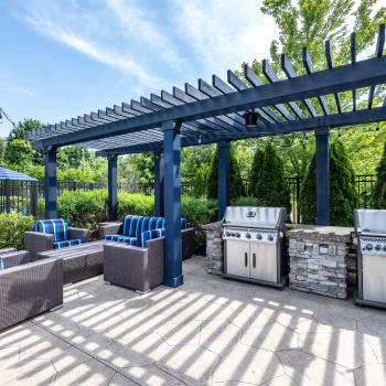 Outdoor grilling station with shaded seating framed by greenery and modern pergola beams