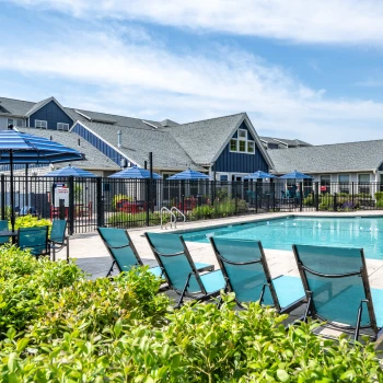 Community swimming pool with teal lounge chairs and black fence surrounding modern clubhouse
