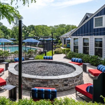 Round outdoor stone firepit surrounded by red and blue cushioned patio lounge chairs