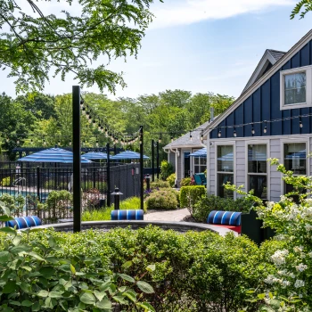 Garden-side clubhouse patio with string lights, blue umbrellas, and cozy seating near pool area
