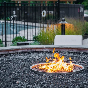 Evening firepit ambiance with soft lighting and fenced-in pool just behind the seating area