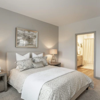 Bedroom with beige and white bedding and view into en-suite bathroom with curtain shower