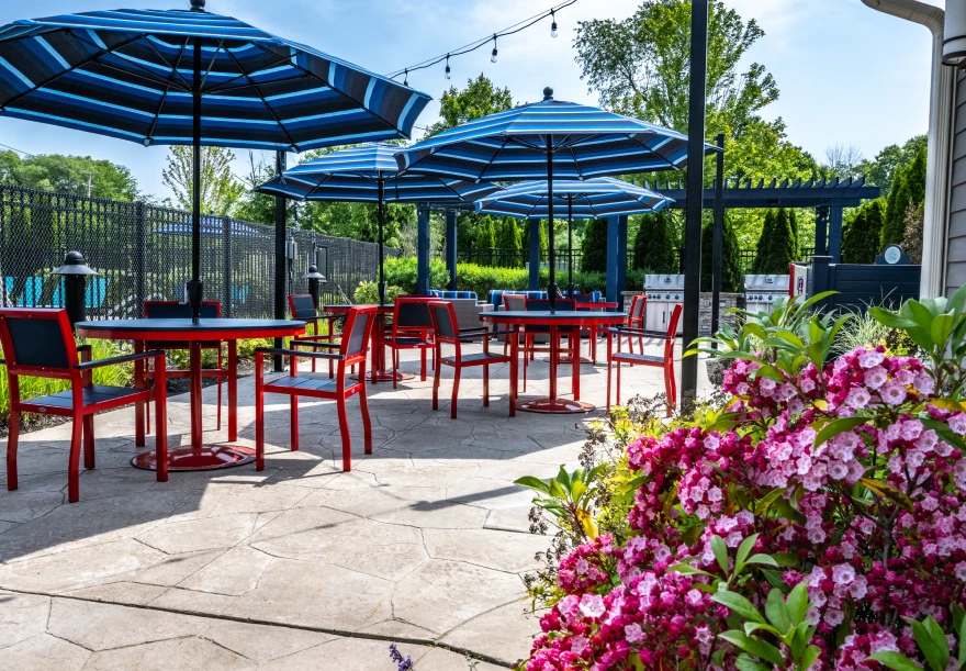 Colorful outdoor patio with red chairs, striped umbrellas, and blooming flowers