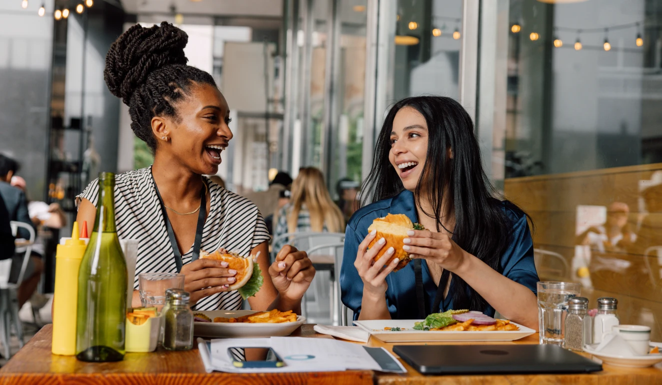 Two women laughing and enjoying burgers together at a modern urban cafe table