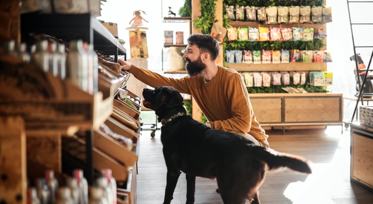 Bearded man with large black dog browsing pet treats in modern pet supply store